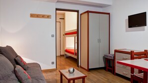 Ein kleines Zimmer mit Etagenbett, Schreibtisch mit Stuhl, Fernseher und einem kleinen Tisch mit einem dekorativen Gegenstand.