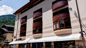 Ein mehrstöckiges Gebäude mit großen Fenstern und Balkonen, das eine gestreifte Fassade und ein weißes Markisenrollo über dem Eingang aufweist.