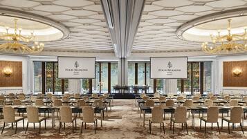 A conference room with a high ceiling, chandeliers, and a large screen displaying the hotel name.