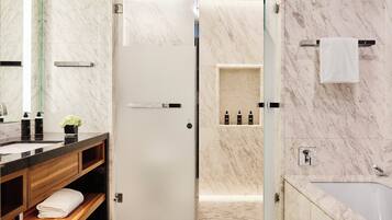 A modern bathroom with a marble floor, a wooden vanity, a glass shower enclosure, and a bathtub.