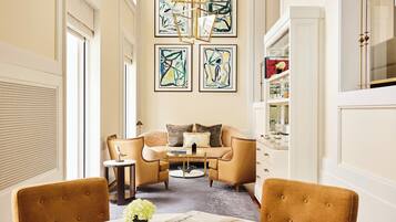 Una sala de estar moderna con un sofá, dos sillones, una mesa de centro y una mesa de comedor con un jarrón de flores. Hay cuadros abstractos en la pared y una lámpara de araña.