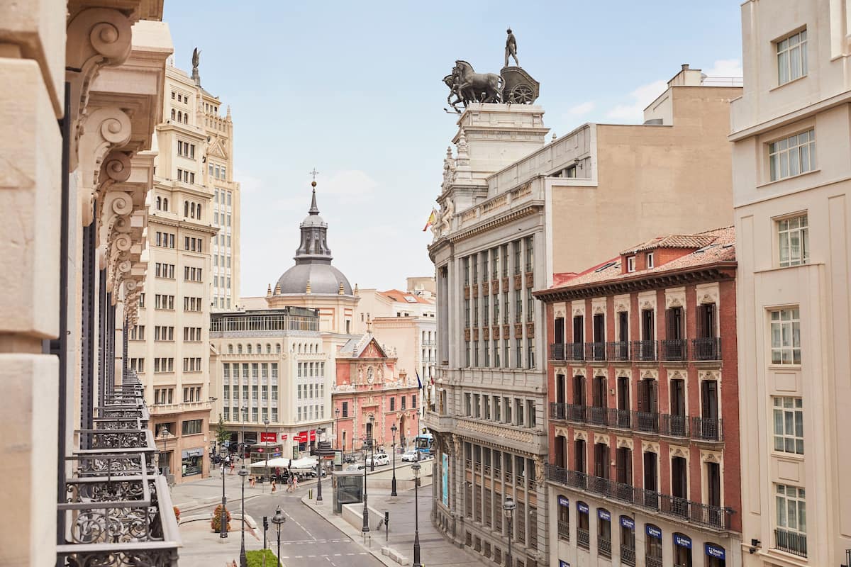 Vista de una calle con edificios históricos, una cúpula destacada y una estatua de un hombre en un carruaje.