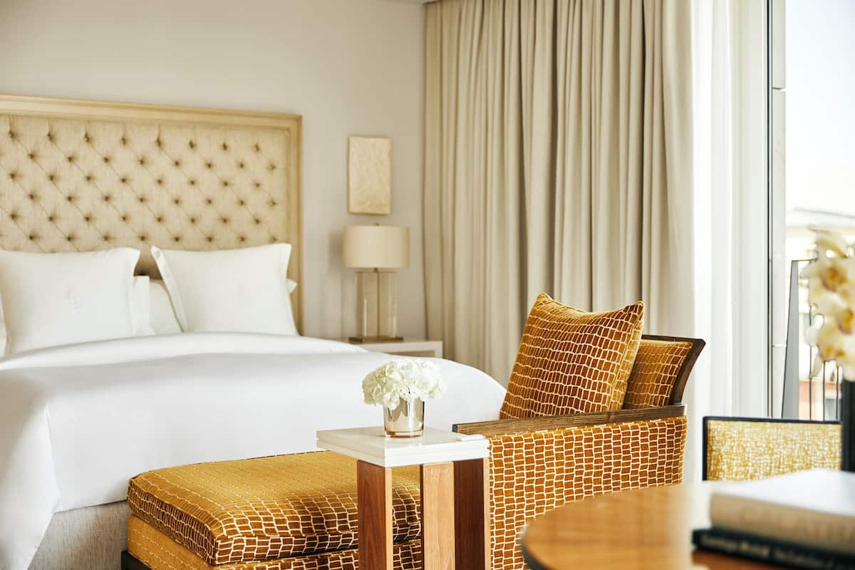 Una habitación de hotel con una cama grande, una mesita de noche con un florero, una silla de mimbre y una lámpara.