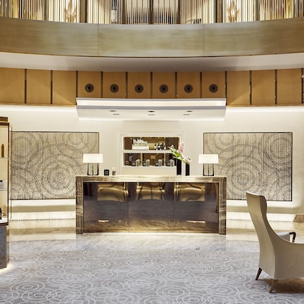 A spacious lobby with a central reception desk, modern chairs, and a patterned floor.