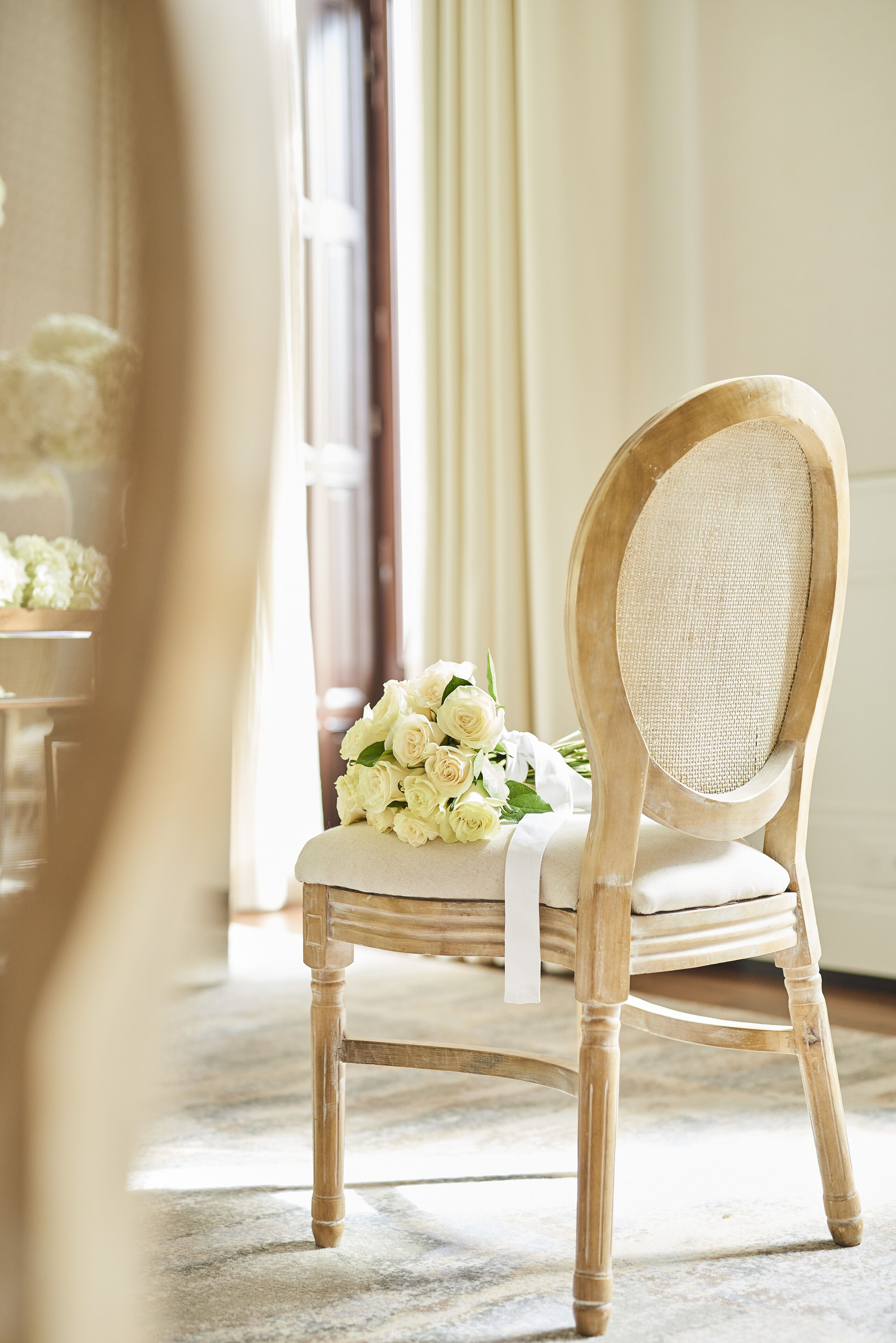 A wooden chair with a cushion and a bouquet of white flowers.
