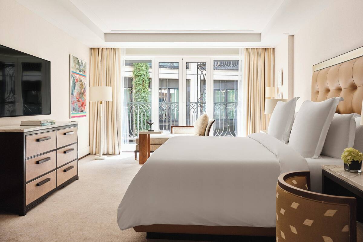Habitación de hotel con una cama grande, un escritorio con lámpara, televisión y vistas al balcón exterior.