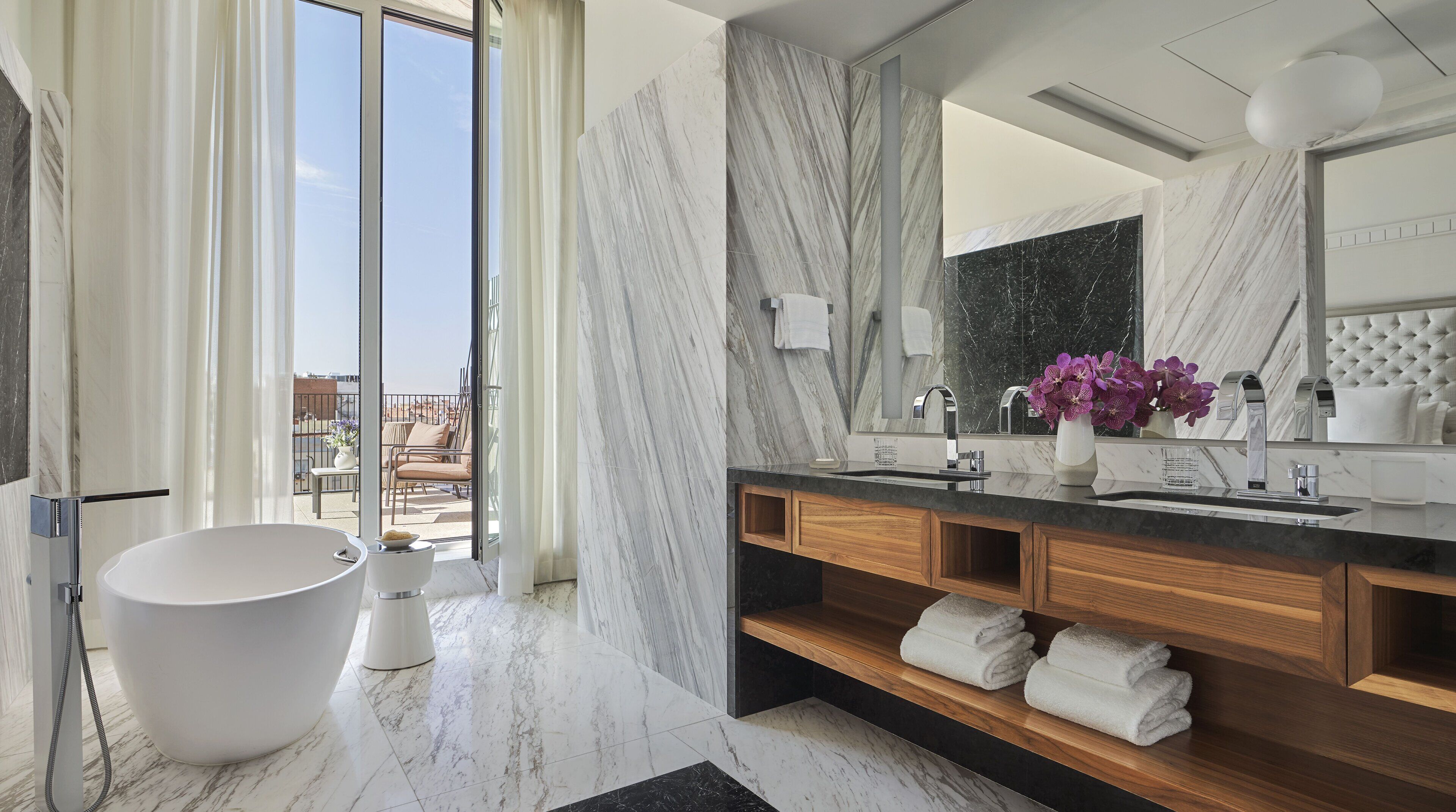 A modern bathroom with a freestanding bathtub, marble walls, and a large mirror.