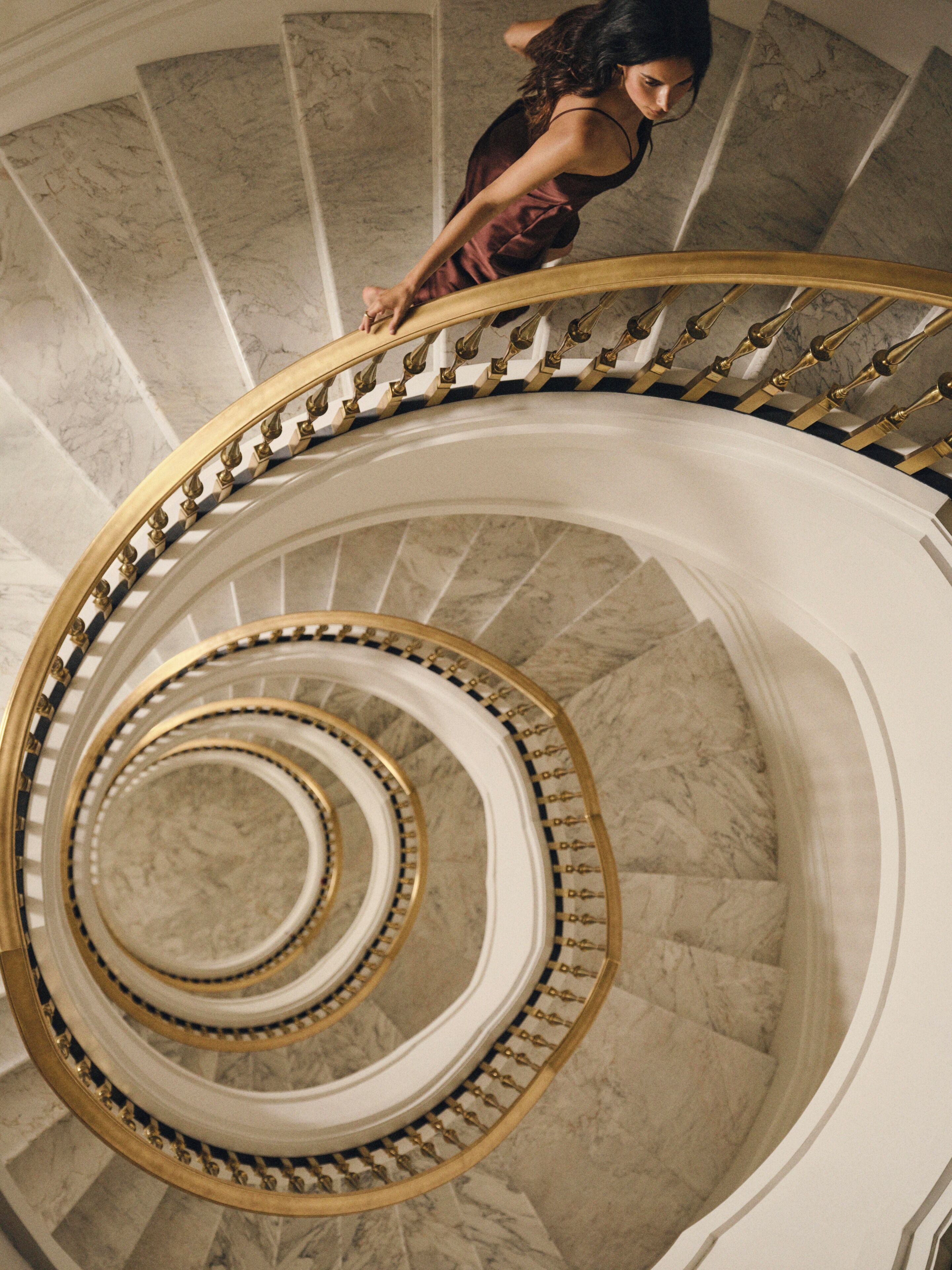 A grand spiral staircase with marble steps and golden balusters.