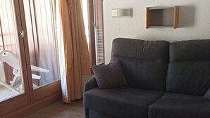 Una sala de estar con un sofá, una mesita y un ventanal corredera.
