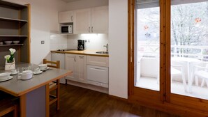 Cocina compacta con armarios blancos, microondas y cafetera. Hay una mesa de comedor con sillas y vistas a un paisaje nevado a través de una puerta de vidrio.