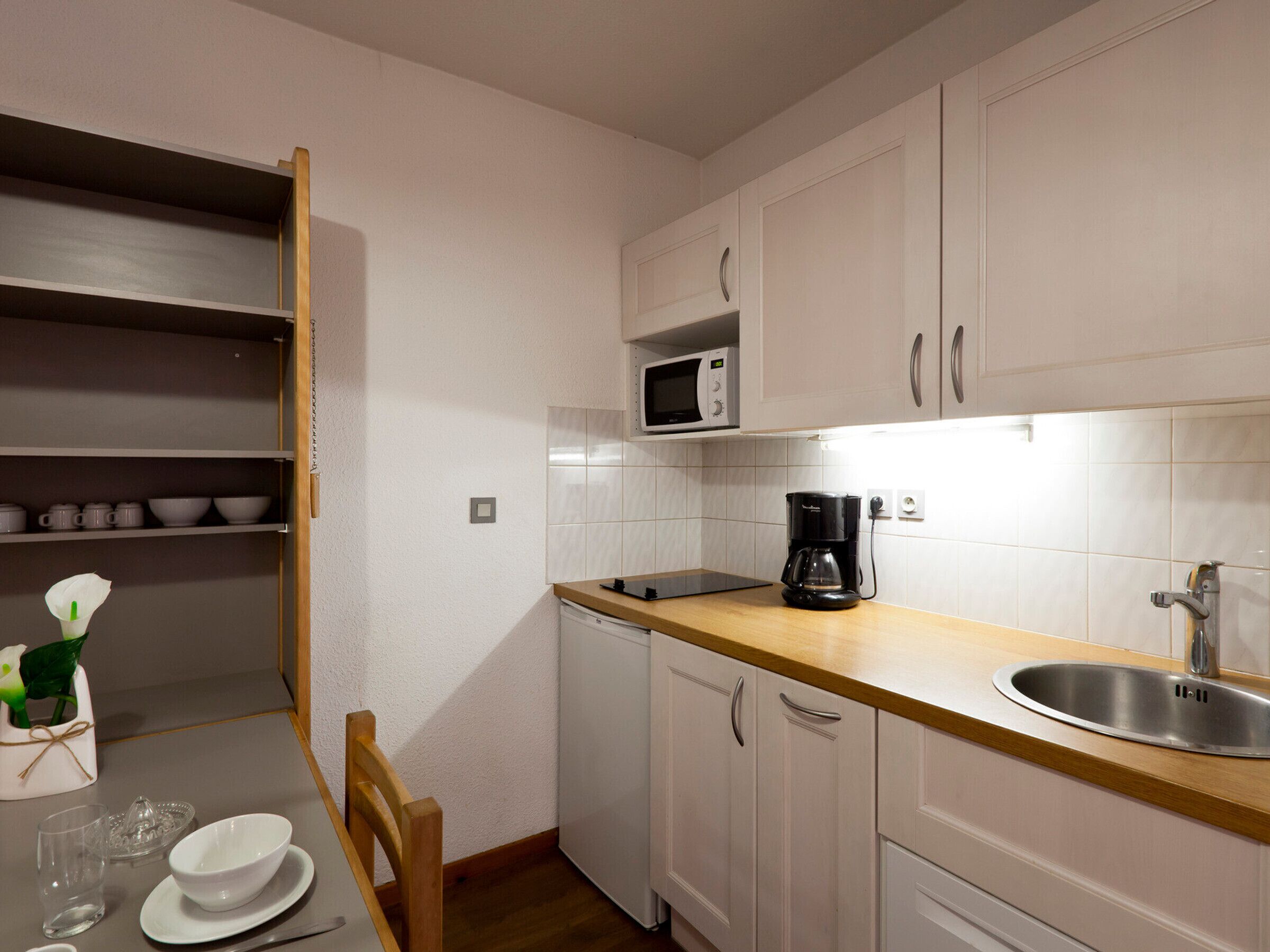 Una cocina pequeña con armarios blancos, microondas, cafetera y lavamanos.
