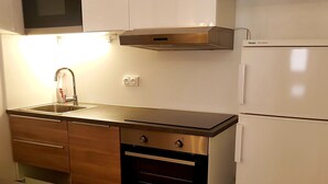 Uma cozinha moderna com pia de aço inoxidável, armários de madeira, forno embutido e geladeira branca.