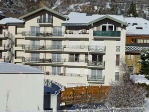 Ein mehrstöckiges Hotel mit Balkonen, einer Skipiste und verschneiter Landschaft.