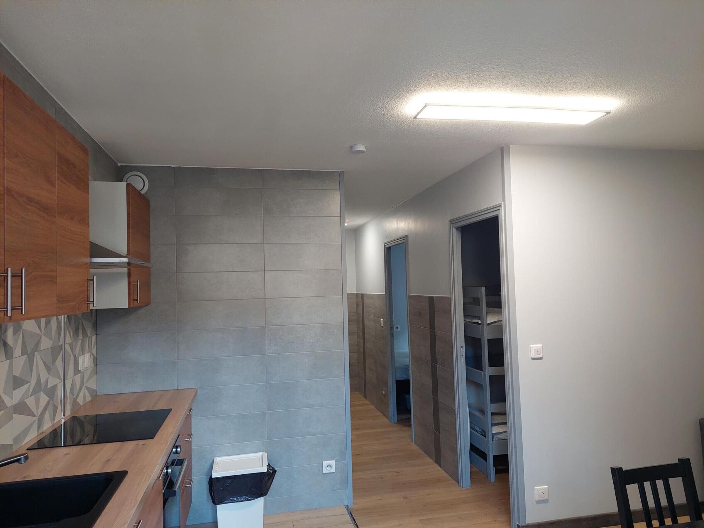 A modern kitchen with wooden cabinets, a built-in stove, and a trash bin.