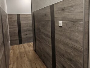 A narrow hallway with wooden flooring and dark grey tiled walls with vertical black stripes.