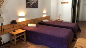 A hotel room with two beds, a wooden nightstand, a lamp, and a wall-mounted picture. - Studio in Brides-les-Bains with Balcony and WiFi (Brides-les-Bains)