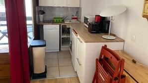 Une cuisine de taille réduite avec des meubles blancs, un lave-vaisselle, un four à micro-ondes et une machine à café.