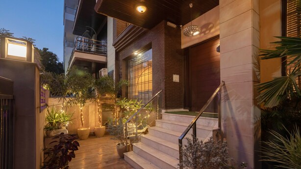 Un edificio moderno con una escalera que lleva a un balcón, rodeado de plantas en macetas e iluminación exterior.