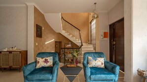 Una sala moderna con dos sillones azules, una pequeña mesa de centro negra y una escalera que conduce a un piso superior.