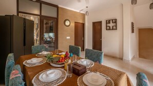 Un comedor con una mesa dispuesta para cuatro personas, un reloj en la pared y un refrigerador al fondo.