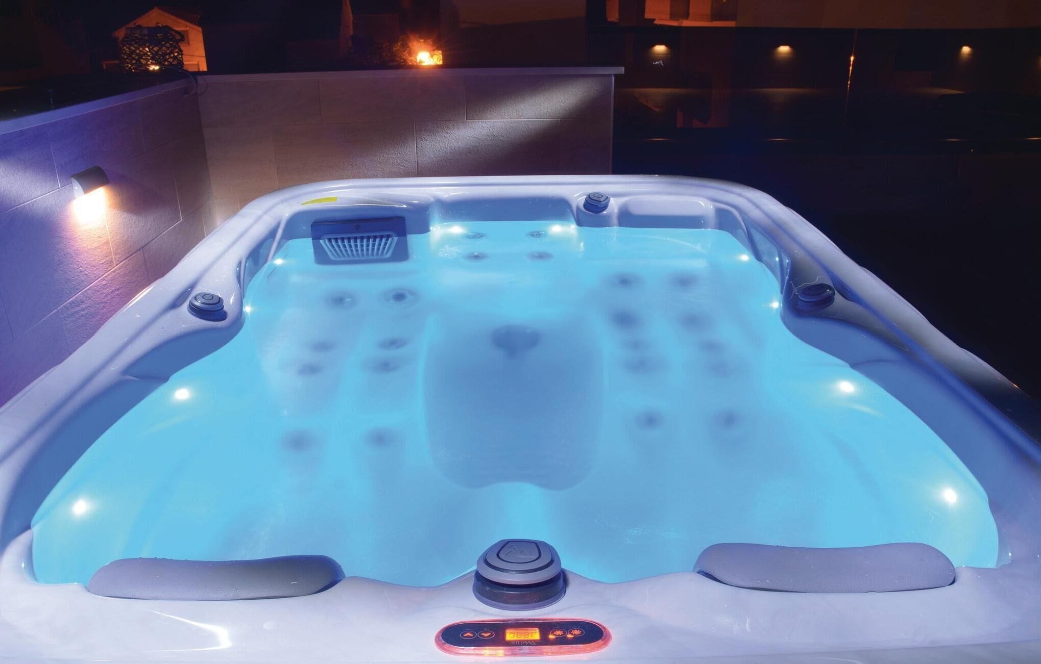 Un jacuzzi con panel de control digital, rodeado por un patio empinado con iluminación ambiental.