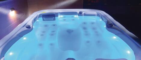 Un jacuzzi con panel de control digital, rodeado por un patio empinado con iluminación ambiental.