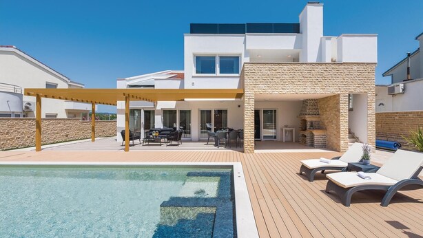 En modern villa med pool, utomhusmöbler och en eldstad i sten.