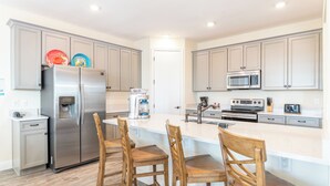 Una cocina moderna con gabinetes grises, electrodomésticos de acero inoxidable y una isla central con taburetes de bar.