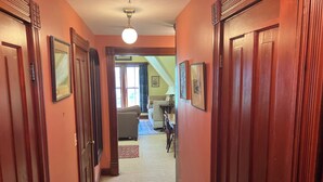 Un couloir avec des portes en bois, un luminaire au plafond et une vue sur un salon avec un canapé et un tapis.