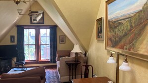 Une pièce mansardée chaleureuse, avec un plafond en pente, une grande peinture, une table à manger en bois et un tapis à motifs.