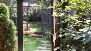 Un sentier de jardin menant à une porte en bois, entouré de verdure et avec une structure en pierre en arrière-plan.