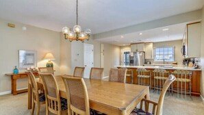 A spacious dining area with a wooden table and chairs, a kitchen in the background, and a chandelier. - Semi OF - CHEVEN at Ships Watch In Duck (Duck)