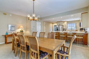 Un comedor espacioso con una mesa y sillas de madera, una cocina al fondo y un candelabro.
