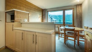 Cocina compacta con muebles de madera, una encimera y un comedor con mesa y sillas. Una ventana ofrece vistas a un paisaje montañoso.