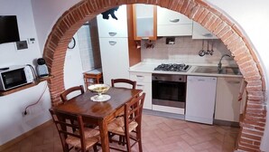 A compact kitchen with a brick archway, white cabinets, a gas stove, and a dining table with chairs. - THE CASINA OF SANT 'AGOSTINO (Colle di Val d'Elsa)