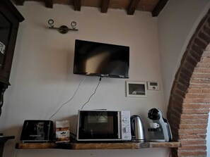 Una cocina con televisión de pantalla plana montada en la pared, microondas, cafetera y tostadora sobre una estantería de madera.