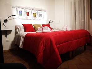 Une chambre d’hôtel avec un lit, une literie rouge, un cadre photo fixé au mur et une lampe de chevet.