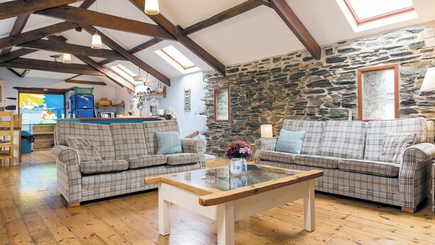 A cozy living room with wooden floors, a stone wall, and a loft-style ceiling with exposed beams. - 3 bedroom accommodation in Menheniot, near Liskeard (Menheniot, near Liskeard)