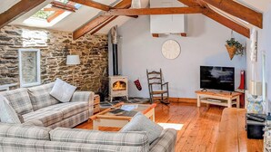 A cozy living room with a stone wall, wooden beams, a fireplace, a television, and a plaid sofa. - 3 bedroom accommodation in Menheniot, near Liskeard (Menheniot, near Liskeard)