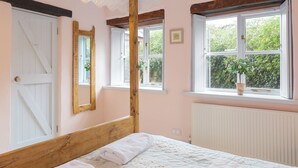 A bedroom with a wooden bed, a white door, and windows with views of greenery. - 3 bedroom accommodation in Menheniot, near Liskeard (Menheniot, near Liskeard)