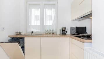 A compact kitchen with a dishwasher, a stove, a microwave, and a window with curtains.
