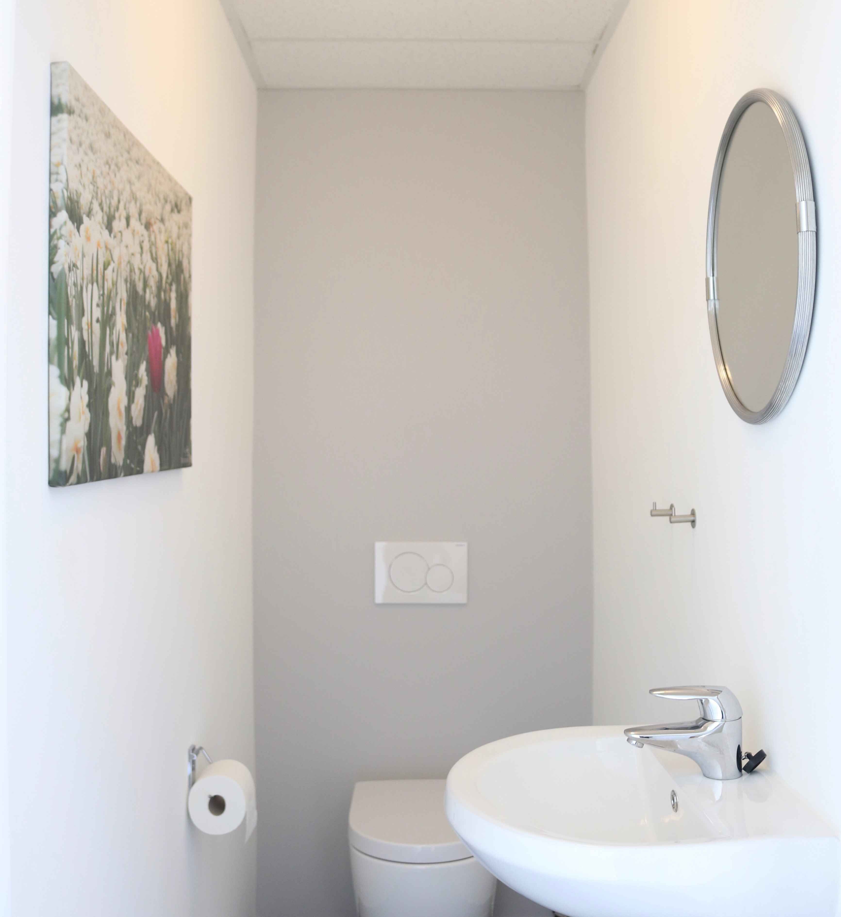 A small, white bathroom with a toilet, a sink, a mirror, and a toilet paper holder.