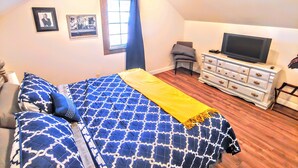 Un dormitorio con cama, televisor, cómoda, silla y ventilador de techo.