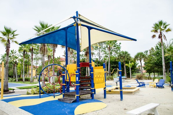 Un parque infantil con estructuras para escalar, toboganes y una zona con sombra.