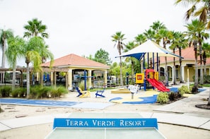 Zona de juegos infantil con tobogán, columpios y un área de descanso cubierta en Terra Verde Resort.