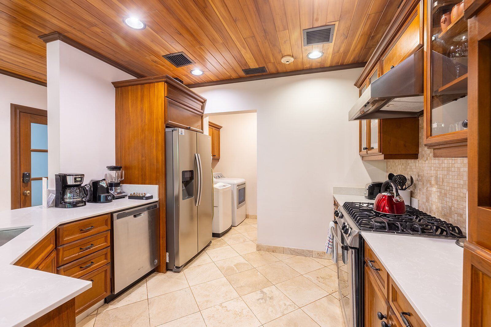 A modern kitchen with wooden cabinets, stainless steel appliances, and a tiled floor.
