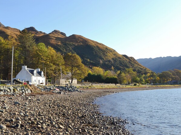 A coastal area with a rocky shoreline, a white building with a boat, and mountains in the background.