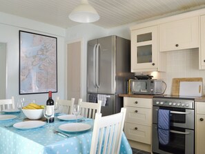 A kitchen with a dining table set for two, a refrigerator, microwave, oven, and a map on the wall.