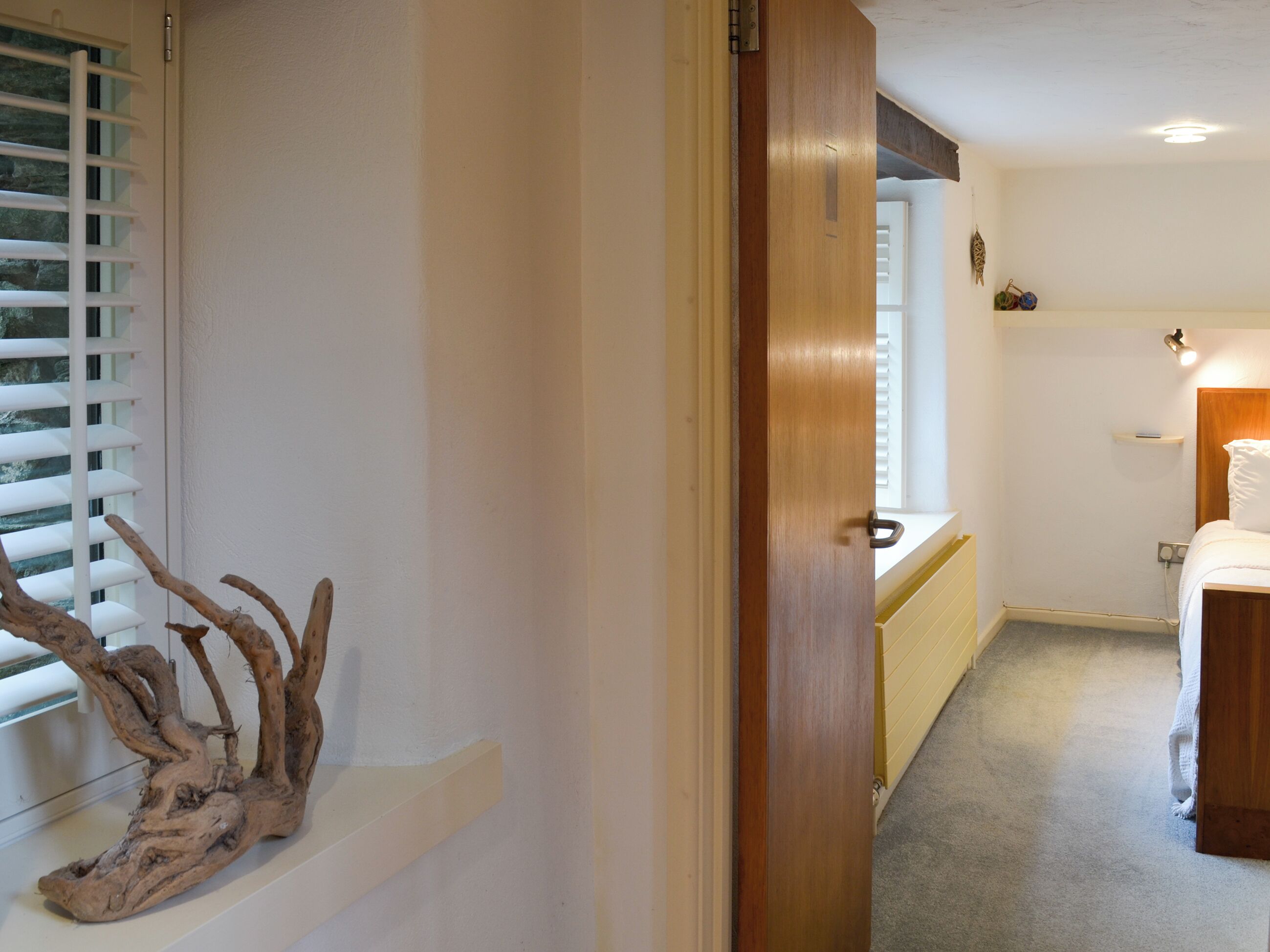 A bedroom with a wooden door, a window with blinds, a bedside table, and a bed.