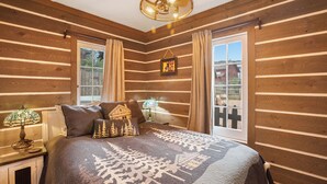 Ein schlafzimmer im Chalet-Stil mit einem Bett, zwei Lampen, einem Bilderrahmen und einem Fenster mit Vorhängen.